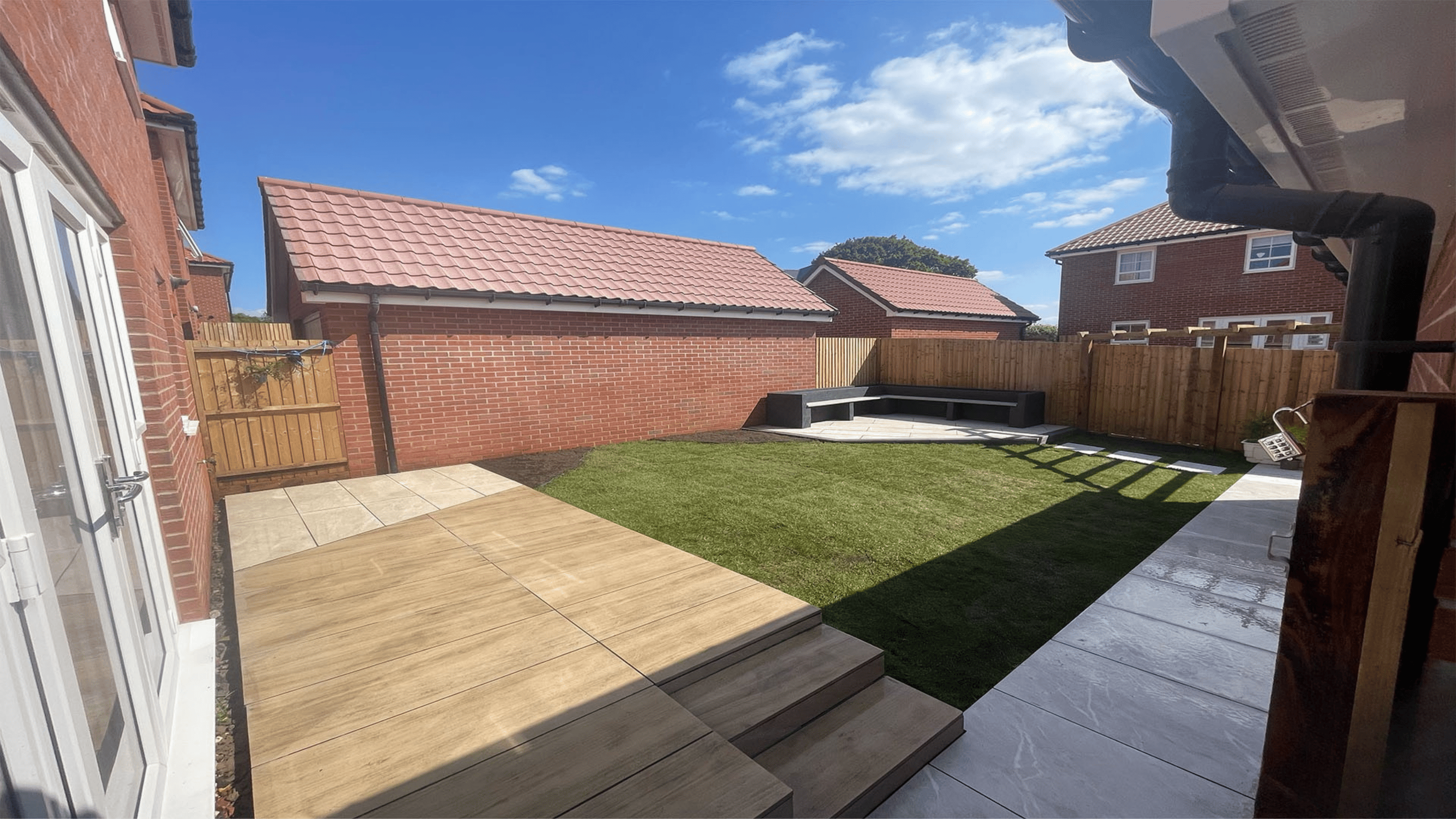 Modern backyard garden design featuring illuminated landscaping with turf lawn, white stepping stones, decorative pebbles, LED-lit trees and custom wooden seating area in Bristol